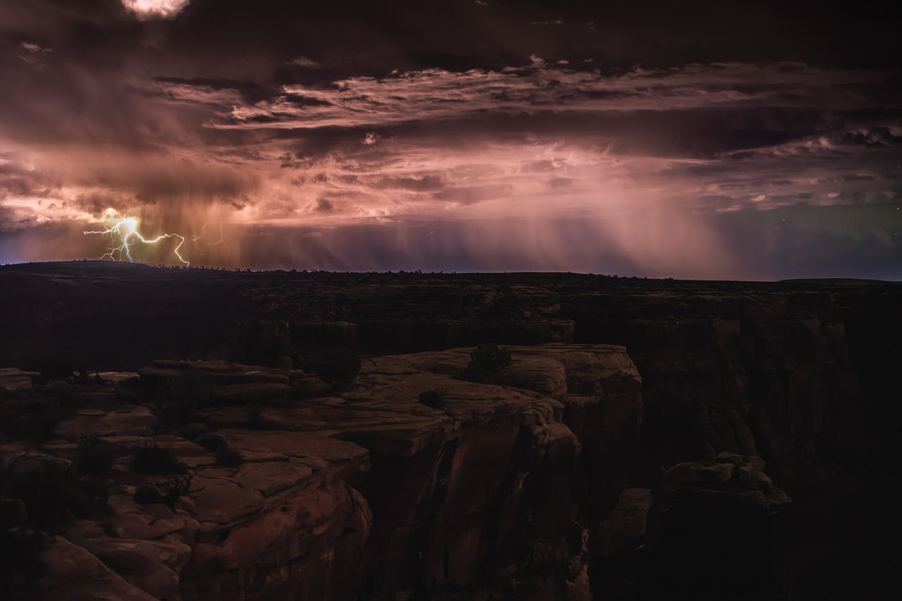 Storm on the horizon with lightning that illuminates the desert and the rain as it falls.